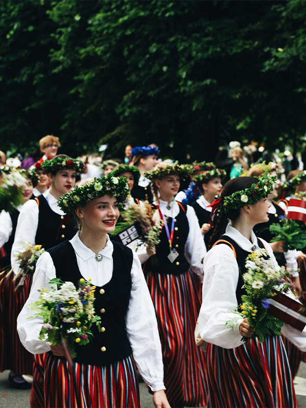 Jeunes femmes en costumes folkloriques lettons traditionnels avec couronnes de fleurs et bouquets sauvages souriantes lors d'un défilé dans les rues de Riga