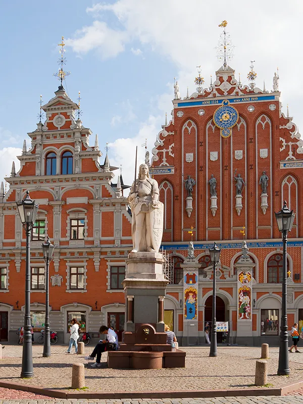 Maison des Têtes-Noires en brique rouge gothique avec la statue de Roland au premier plan sur la place de l'Hôtel de Ville de Riga par une après-midi ensoleillée