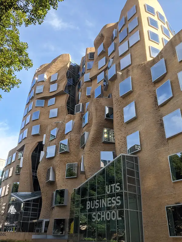 Façade sculpturale en briques de l'UTS Business School avec fenêtres miroirs irrégulières et entrée vitrée à Sydney