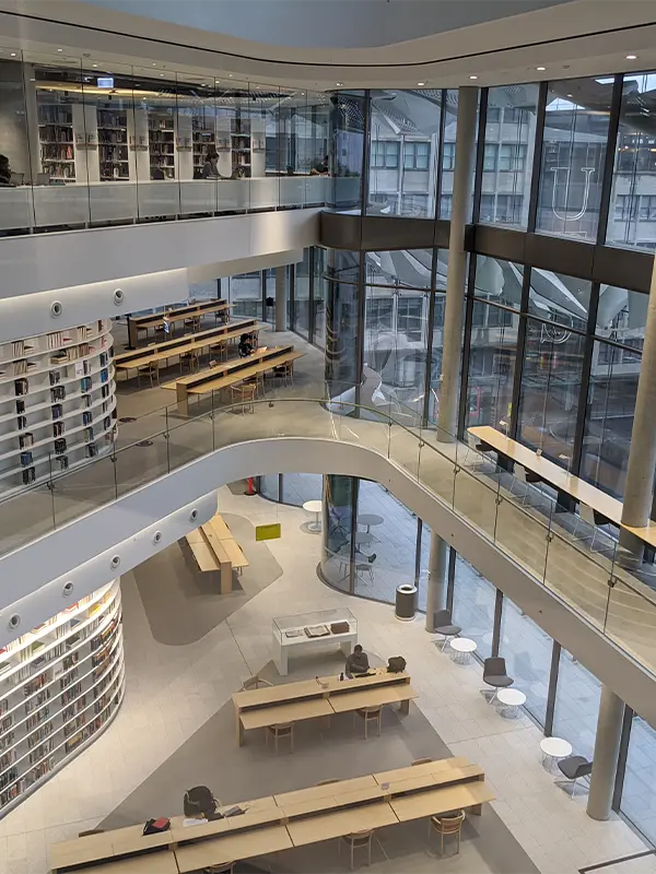 Bibliothèque sur plusieurs niveaux à l'UTS avec balcons vitrés courbés, tables de travail et rayonnages face à la ville