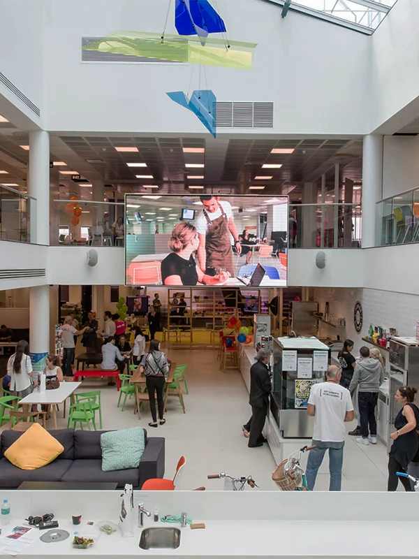 Atrium animé de la Torrens University avec chaises colorées, grand écran LED et installations artistiques suspendues au plafond pendant que des étudiants se retrouvent sur plusieurs niveaux